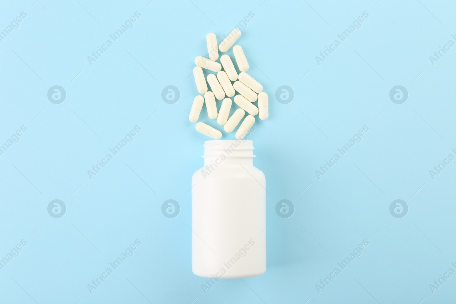 Photo of Bottle and vitamin capsules on light blue background, top view