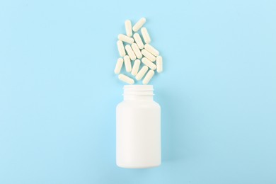 Bottle and vitamin capsules on light blue background, top view