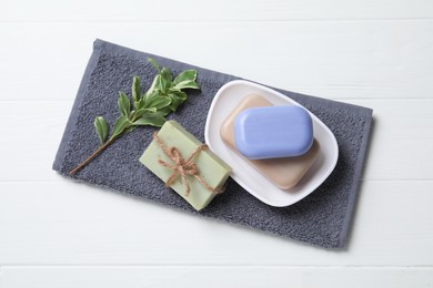 Photo of Different soap bars, plant and terry towel on white wooden table, top view