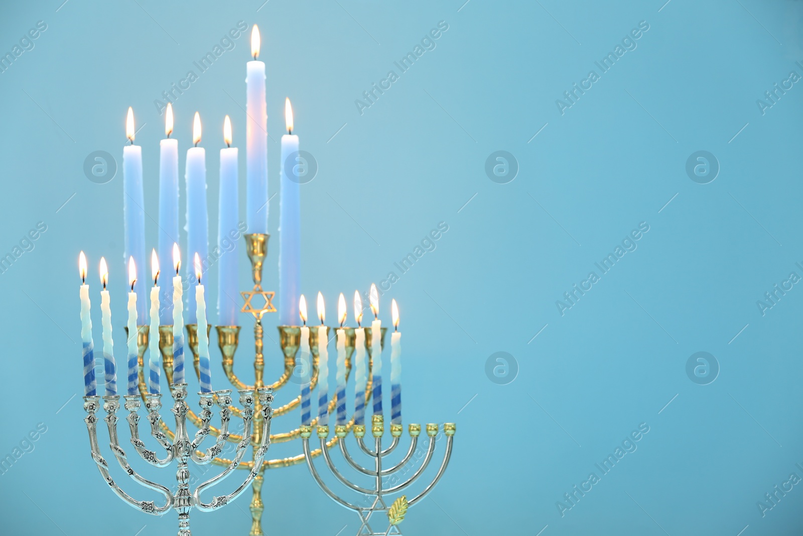 Photo of Hanukkah celebration. Menorahs with burning candles on light blue background, space for text