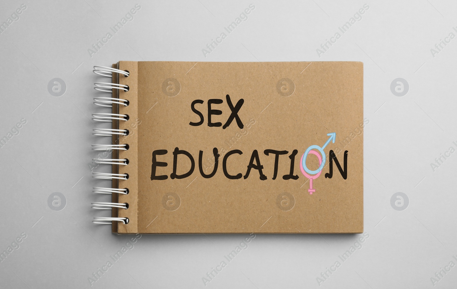 Image of Text Sex Education with female and male gender signs instead of letter O in notebook on light background, top view