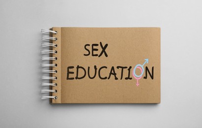 Image of Text Sex Education with female and male gender signs instead of letter O in notebook on light background, top view