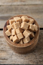 Photo of Brown sugar cubes in bowl on wooden table, closeup