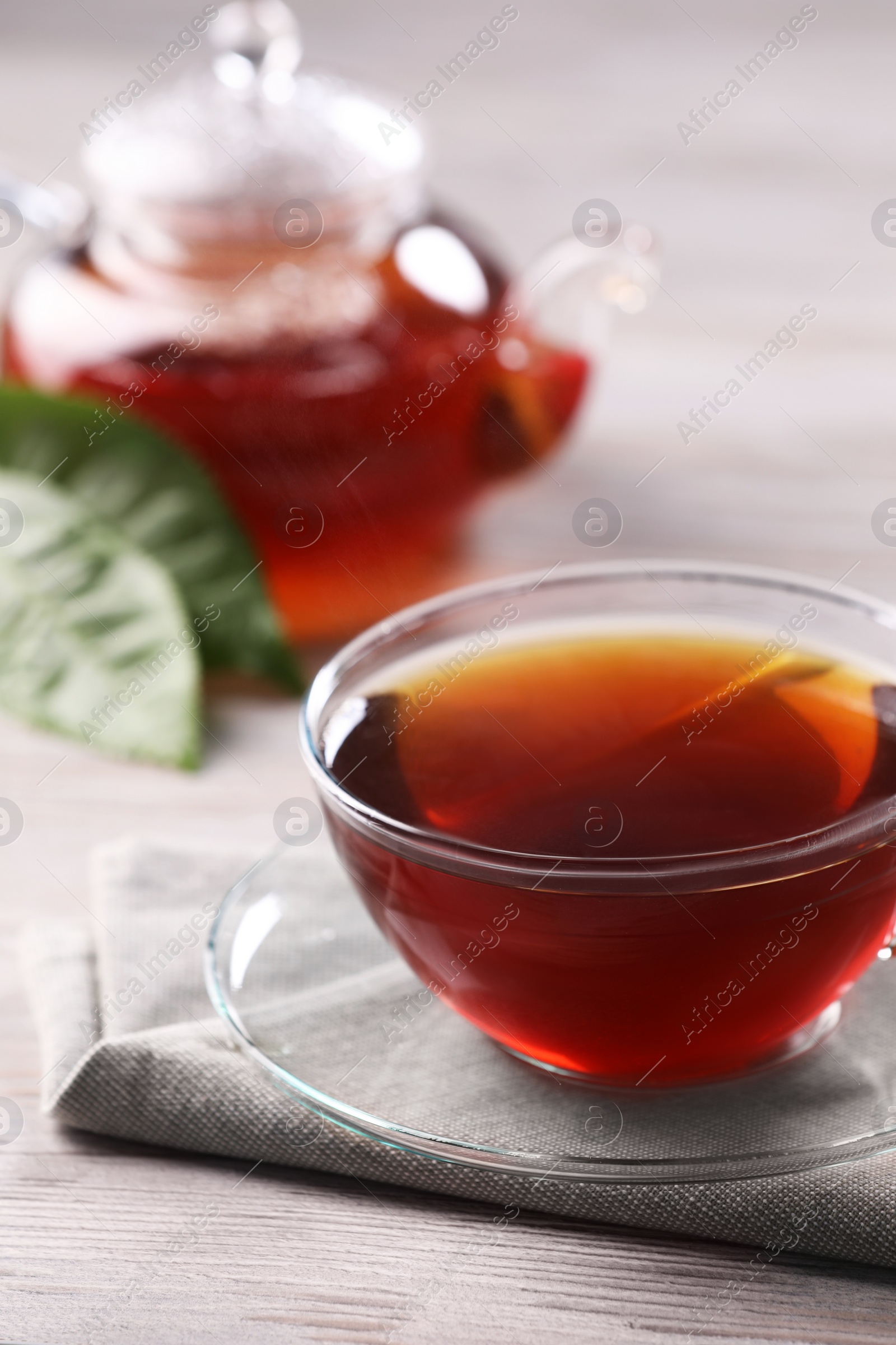 Photo of Fresh hot tea in glass cup, teapot and leaves on white wooden table