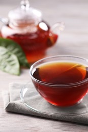 Fresh hot tea in glass cup, teapot and leaves on white wooden table