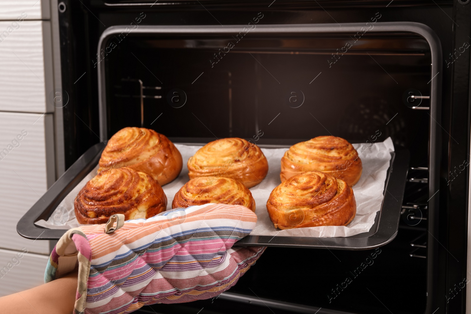 Photo of Woman taking freshly baked buns out of oven, closeup