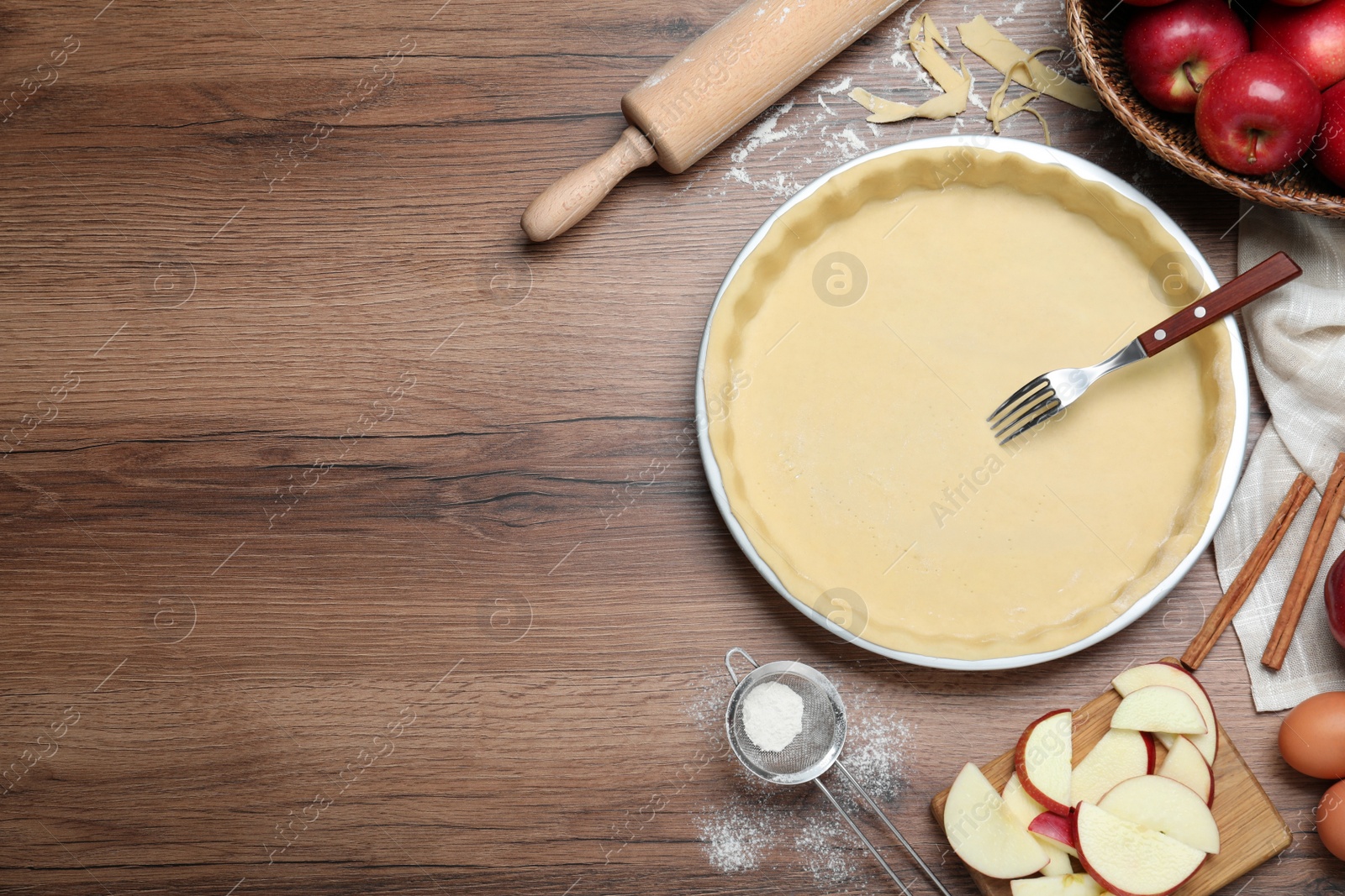 Photo of Flat lay composition with raw dough, fork and ingredients on wooden table, space for text. Baking apple pie