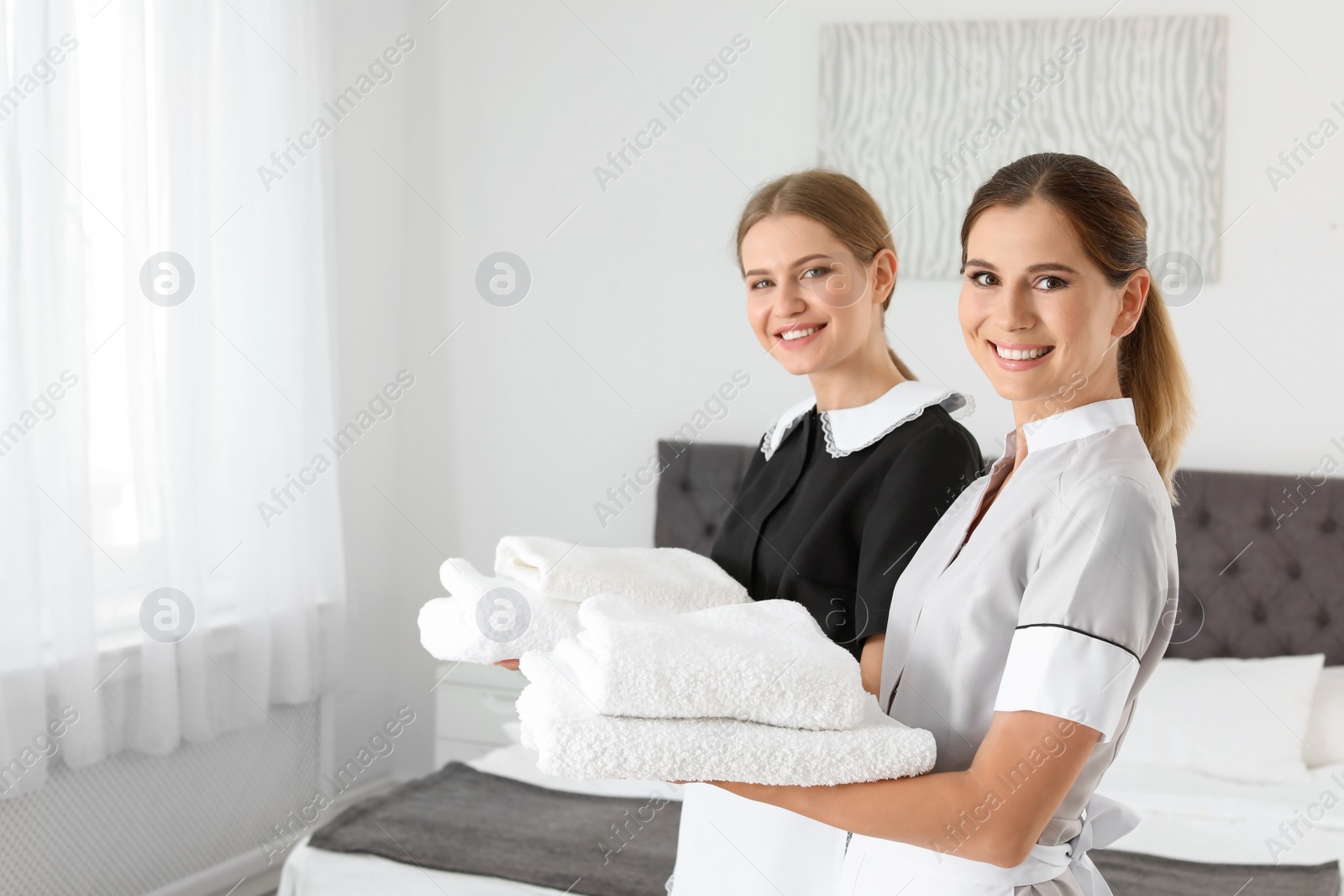 Photo of Professional chambermaids holding clean towels in bedroom