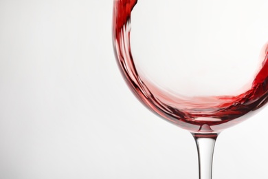 Pouring red wine into glass on light background, closeup