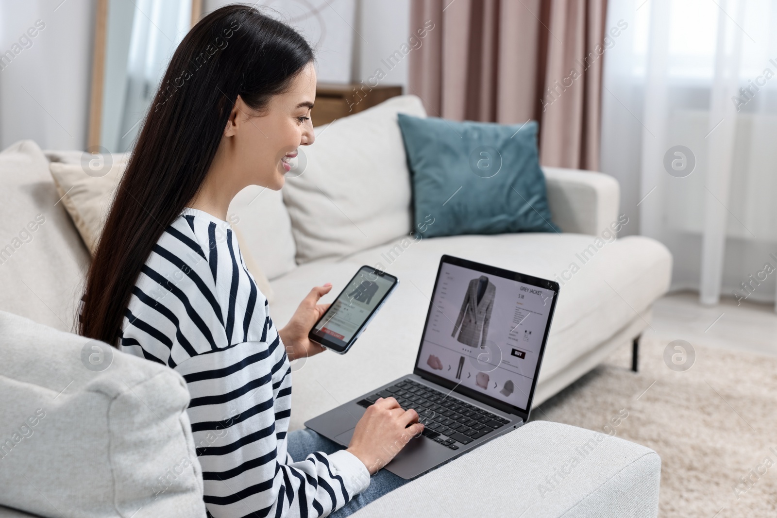 Photo of Beautiful young woman with smartphone and laptop shopping online at home