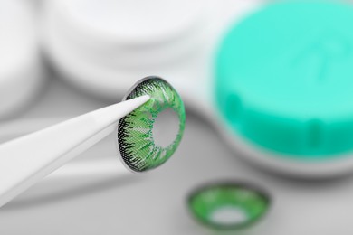 Photo of Tweezers with green contact lens on blurred background, closeup. Space for text