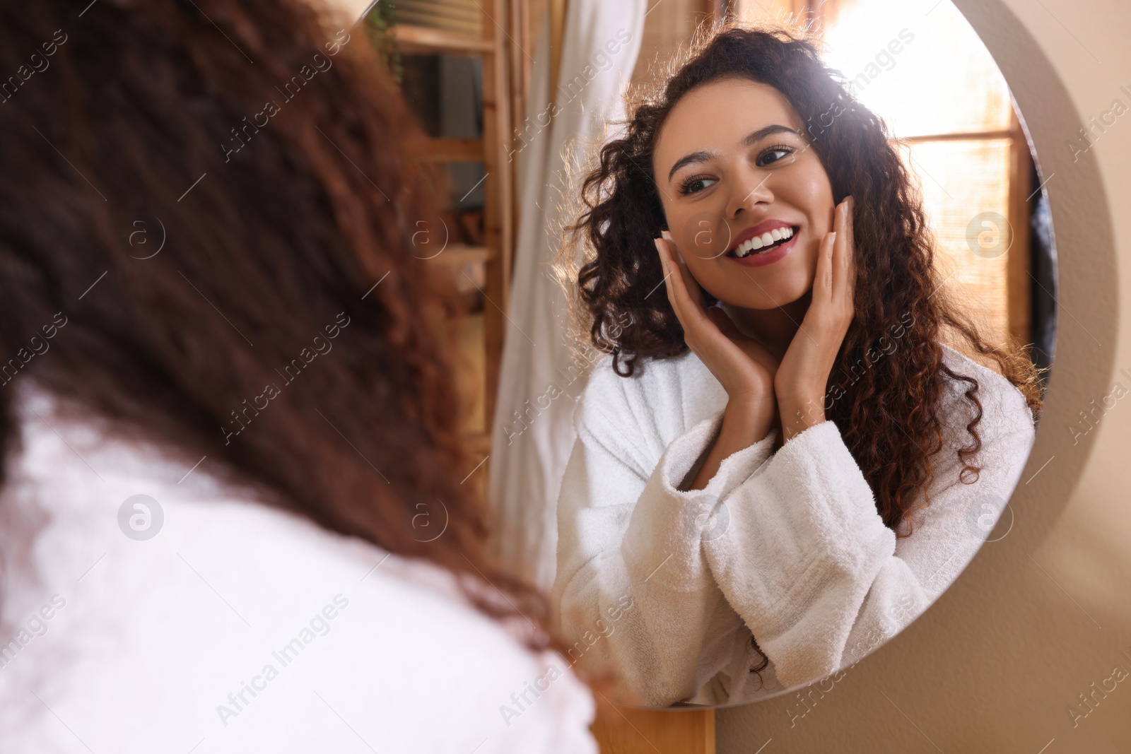 Photo of Beautiful African American woman in bathrobe near mirror at home