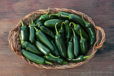 Photo of Wicker basket with green jalapeno peppers on wooden table, top view