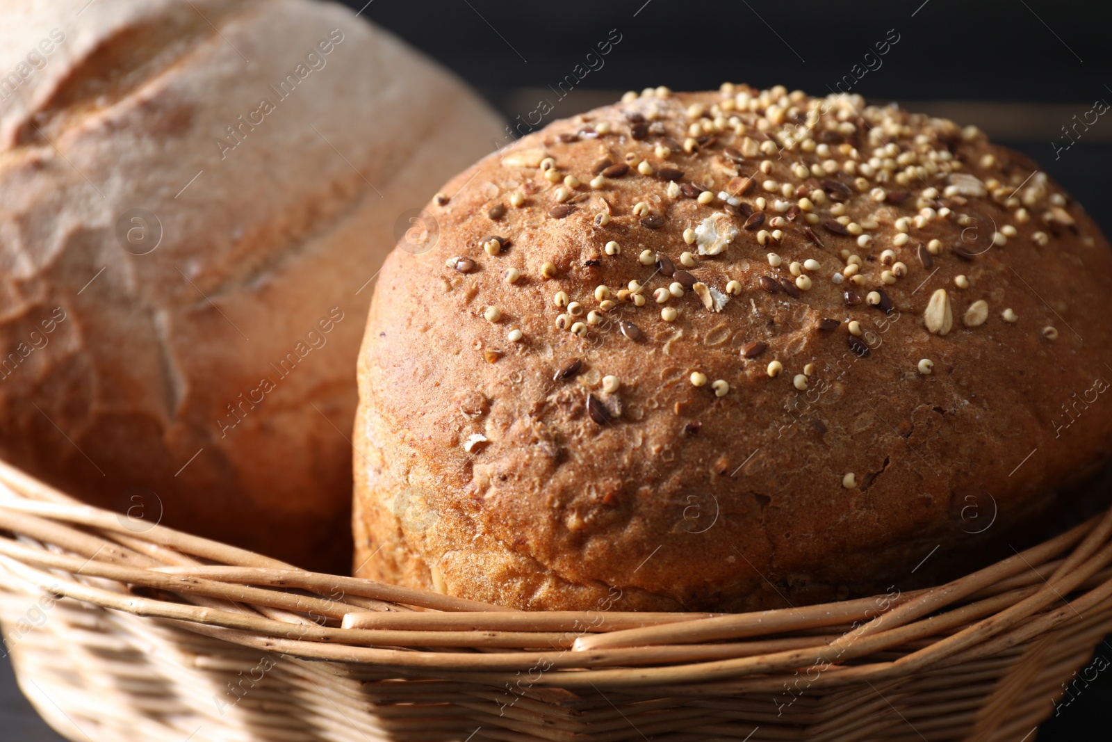 Photo of Wicker basket with fresh bread on dark background, closeup