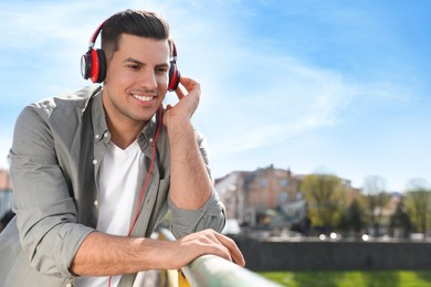 Photo of Handsome man with headphones listening to music outdoors on sunny day, space for text