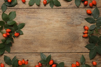Photo of Frame of ripe rose hip berries with green leaves on wooden table, flat lay. Space for text