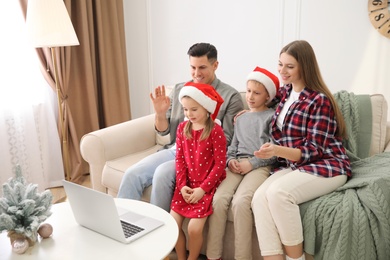 Photo of Family with children using video chat on laptop in room decorated for Christmas