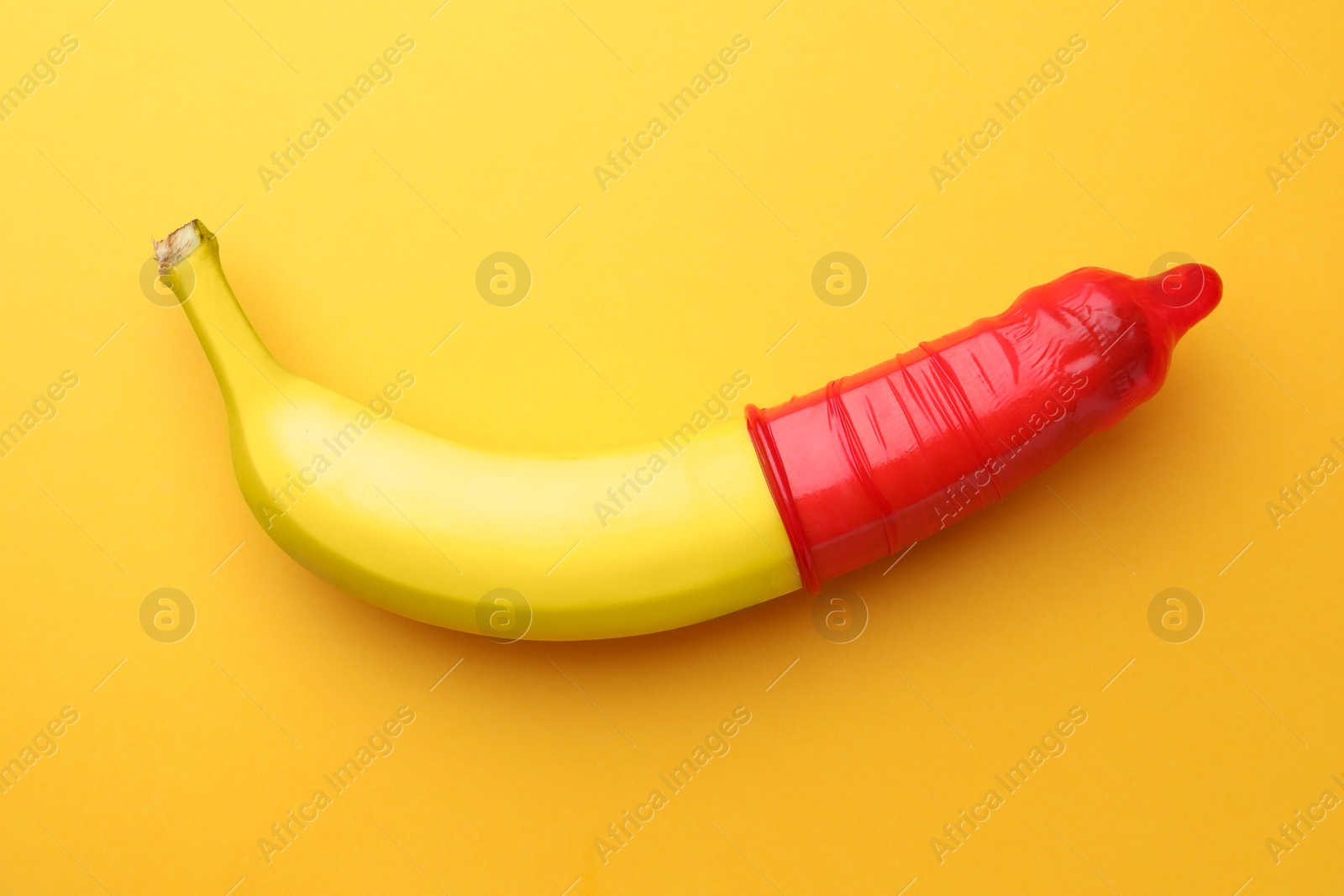 Photo of Banana with condom on orange background, top view. Safe sex concept