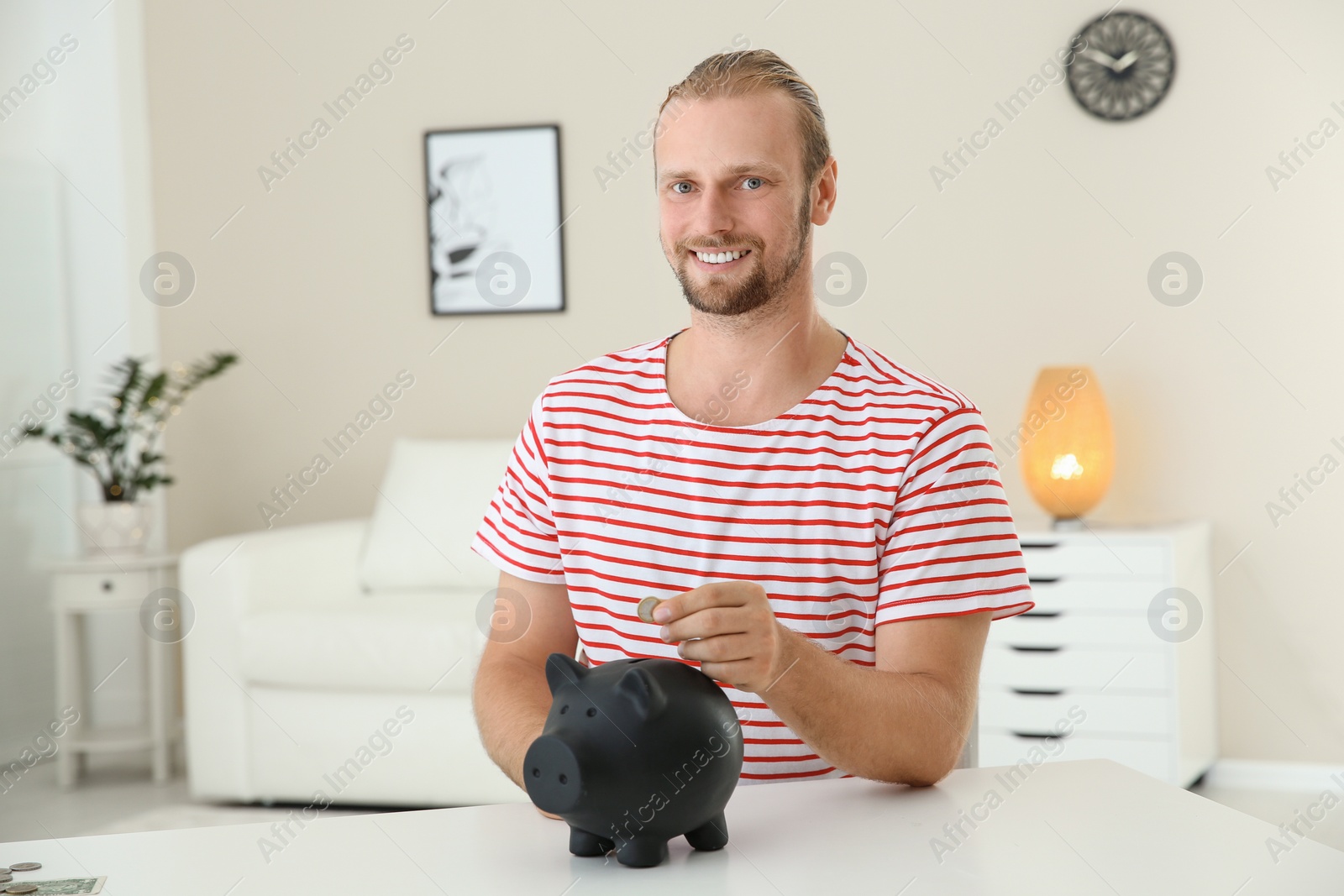 Photo of Man putting coin into piggy bank on table indoors