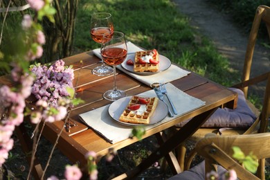 Photo of Delicious Belgian waffles with fresh strawberries and wine served on table in spring garden