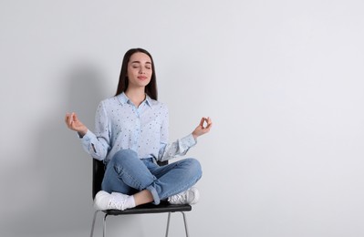 Young woman meditating on chair near white wall in office, space for text