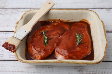 Photo of Raw marinated meat, rosemary and basting brush on white wooden table, closeup