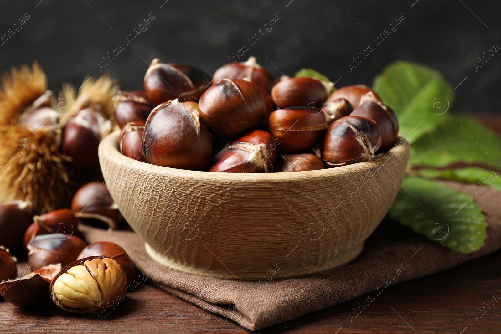 Photo of Delicious roasted edible chestnuts in wooden bowl on table, closeup