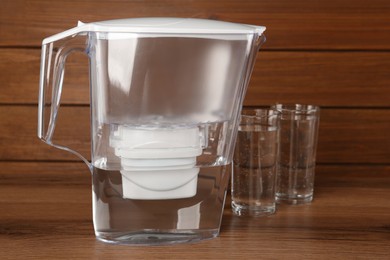 Filter jug and glasses with purified water on wooden table