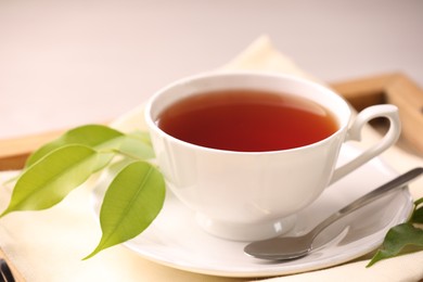 Photo of Aromatic tea in cup, saucer, spoon and green leaves on table, closeup