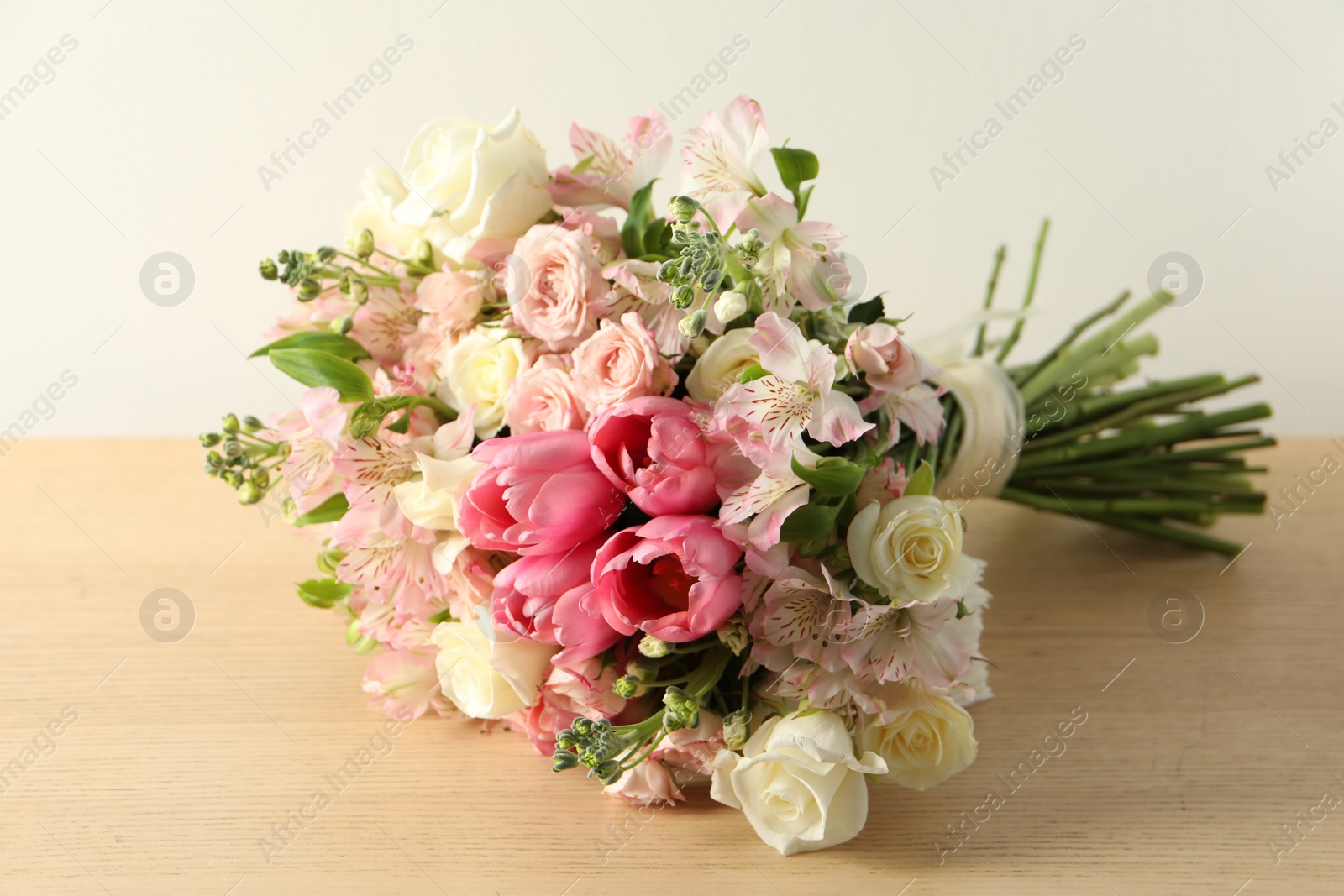 Photo of Beautiful bouquet of fresh flowers on wooden table near light wall