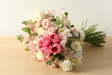 Beautiful bouquet of fresh flowers on wooden table near light wall