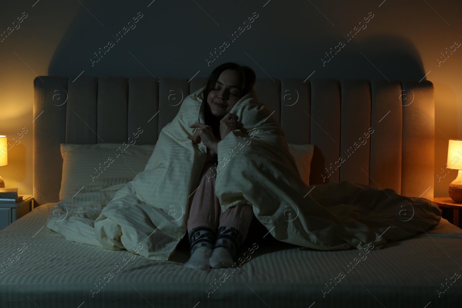 Photo of Woman with blanket warming in cozy bedroom at night