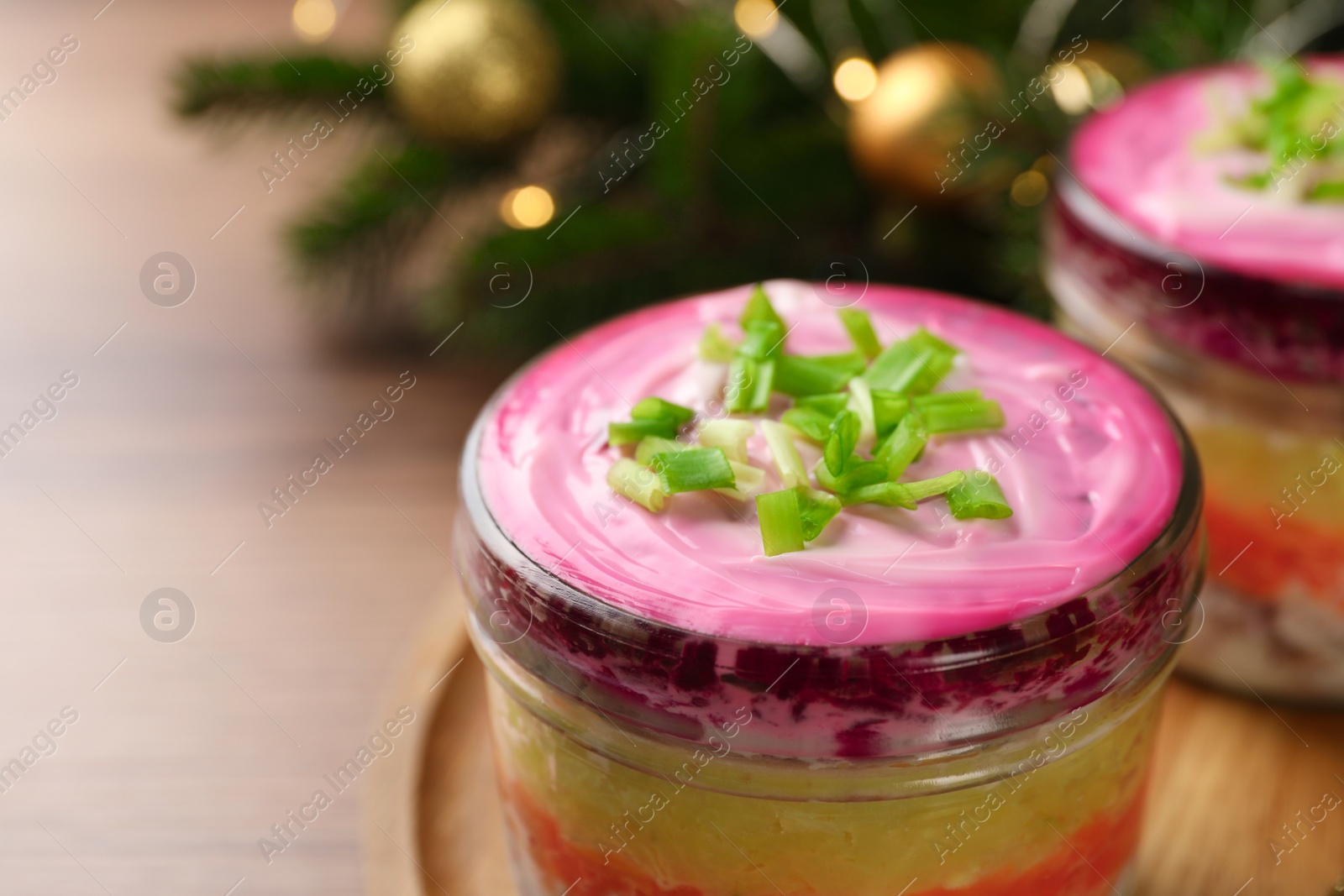 Photo of Glass jars of herring under fur coat and Christmas decor on wooden table, closeup with space for text. Traditional Russian salad