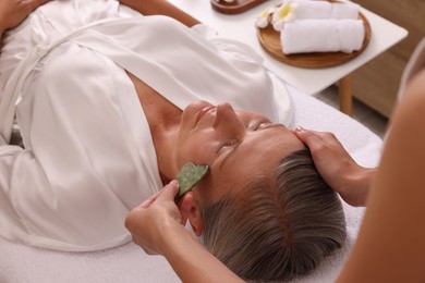 Photo of Woman receiving facial massage with jade gua sha tool in beauty salon, closeup