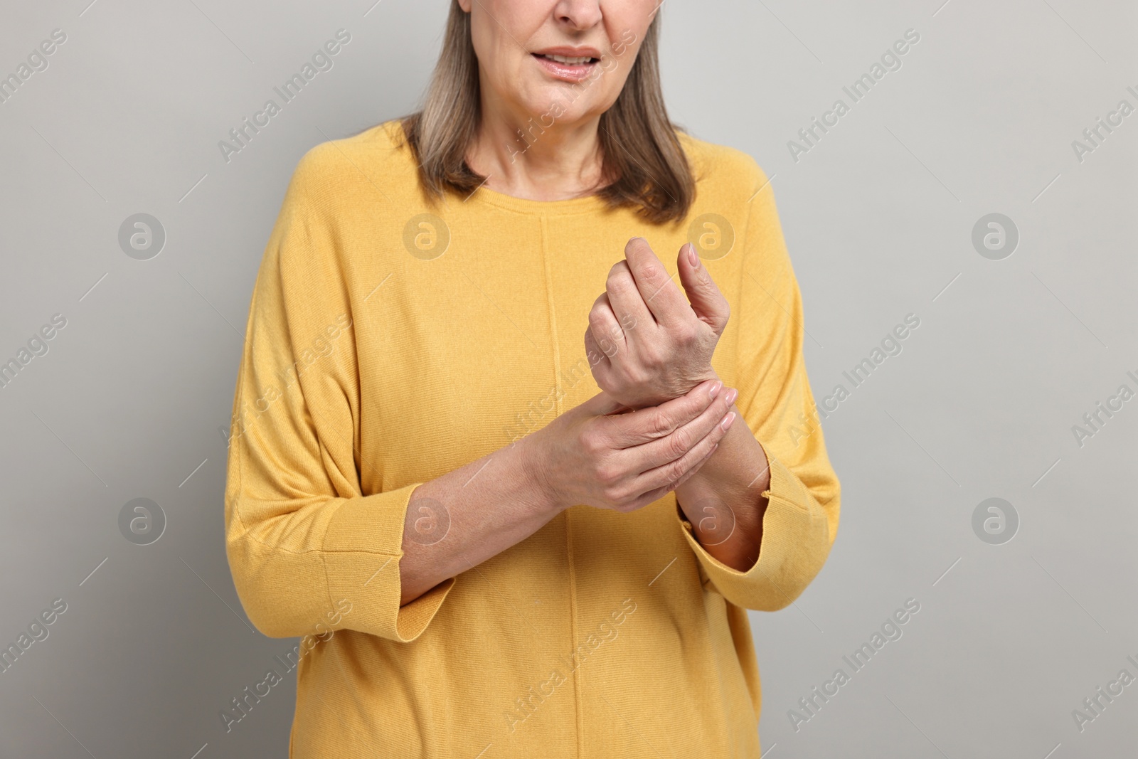 Photo of Arthritis symptoms. Woman suffering from pain in wrist on gray background, closeup