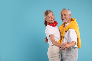 Senior couple dancing together on light blue background, space for text