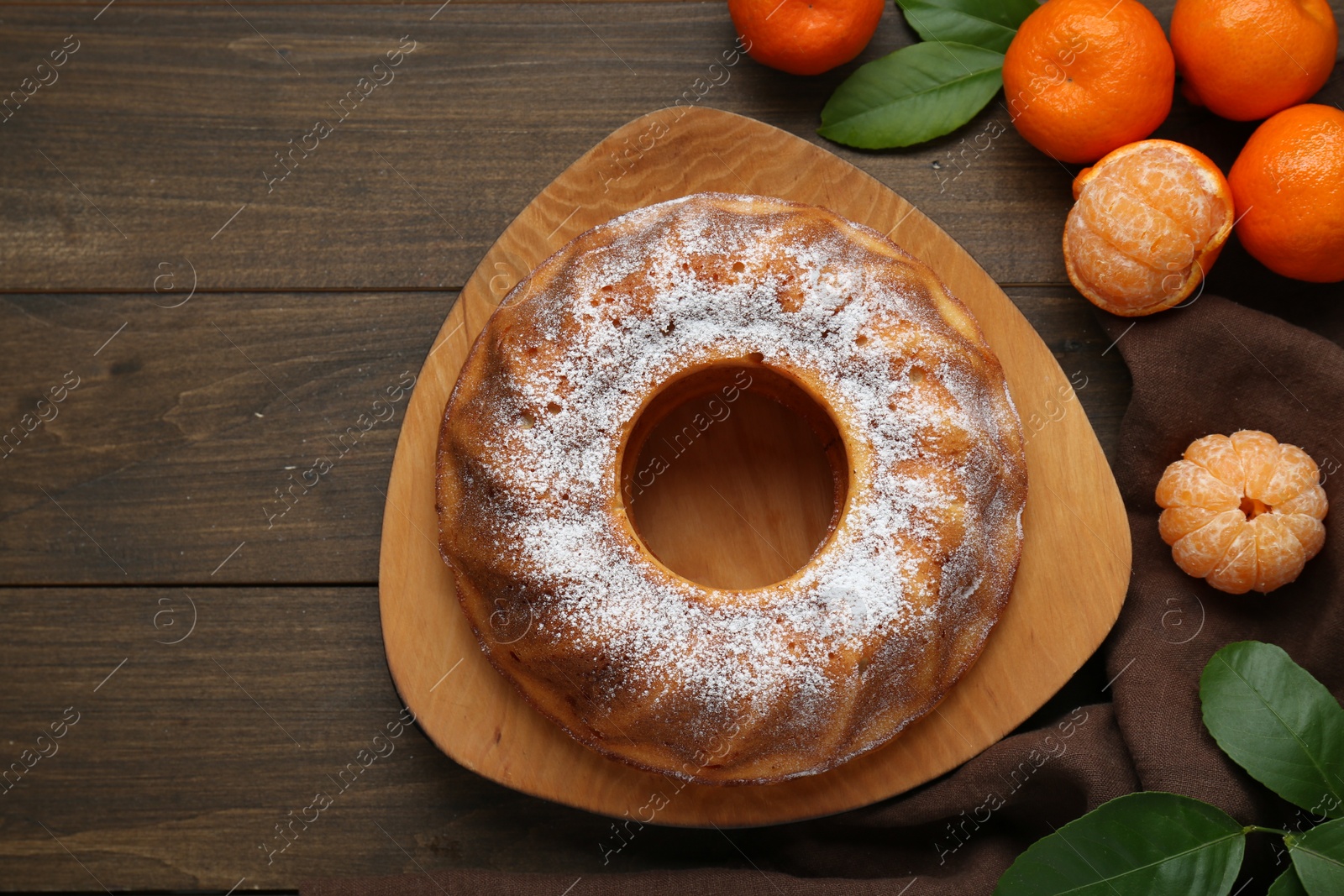 Photo of Homemade yogurt cake with tangerines, powdered sugar and green leaves on wooden table, flat lay. Space for text