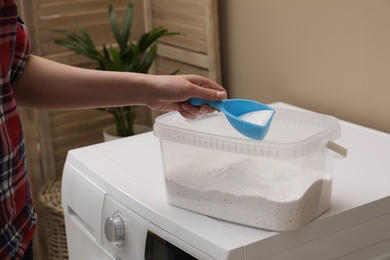 Woman with detergent powder near washing machine in laundry room, closeup