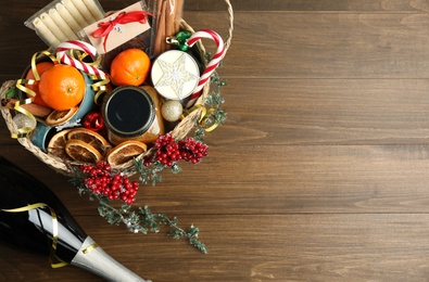 Photo of Wicker basket with gift set, sparkling wine and Christmas decor on wooden table, flat lay. Space for text