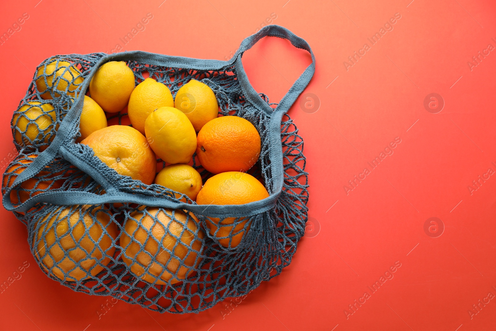 Photo of String bag with oranges and lemons on red background, top view. Space for text