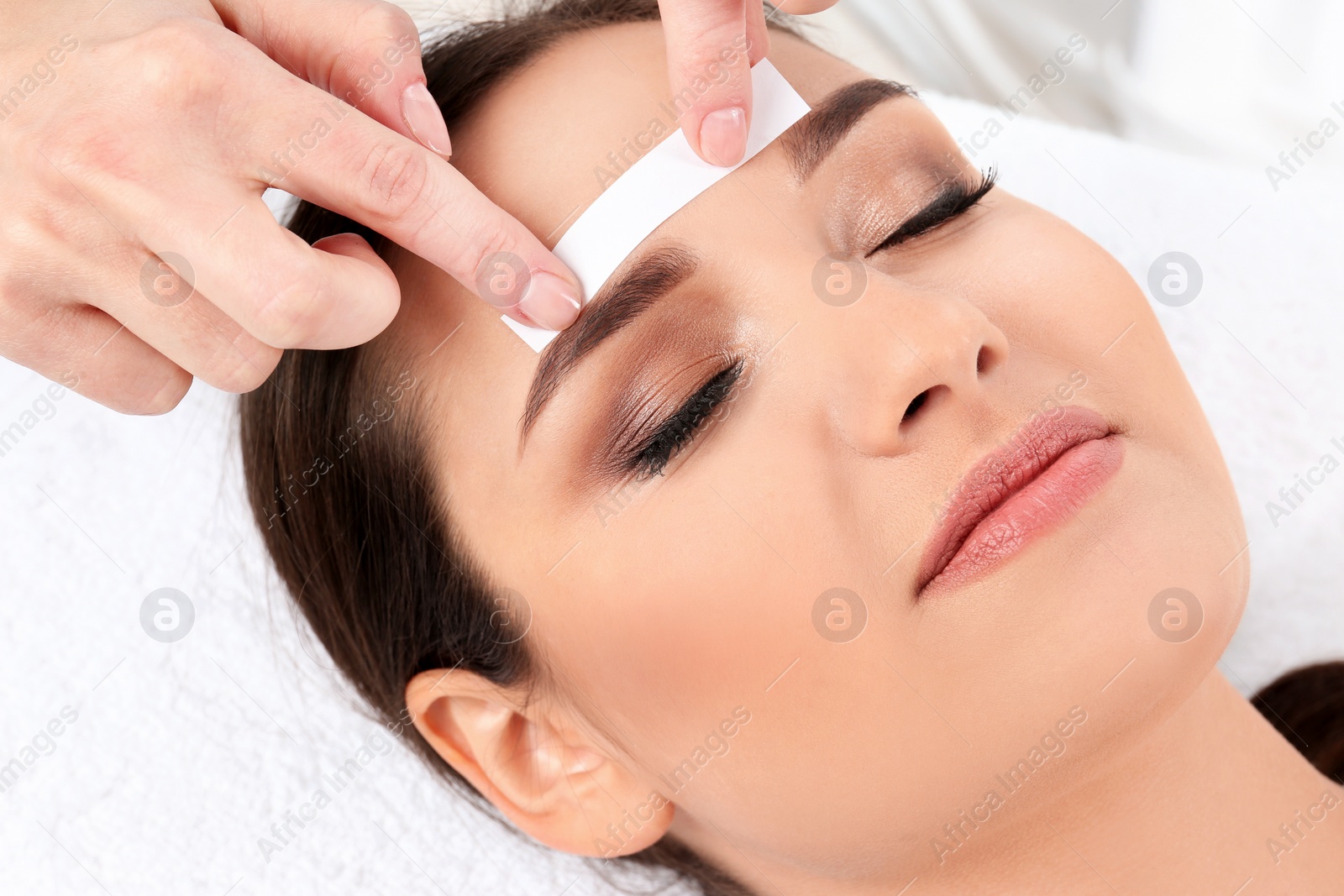 Photo of Young woman having professional eyebrow correction procedure in beauty salon