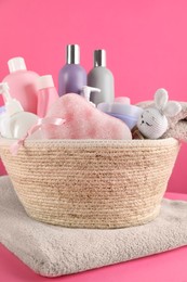 Photo of Wicker basket full of different baby cosmetic products, bathing accessories and toy on pink background