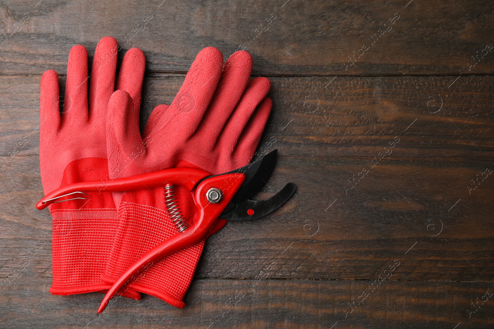 Photo of Pair of red gardening gloves and secateurs on wooden table, top view. Space for text