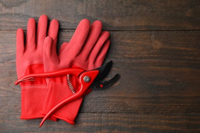 Pair of red gardening gloves and secateurs on wooden table, top view. Space for text