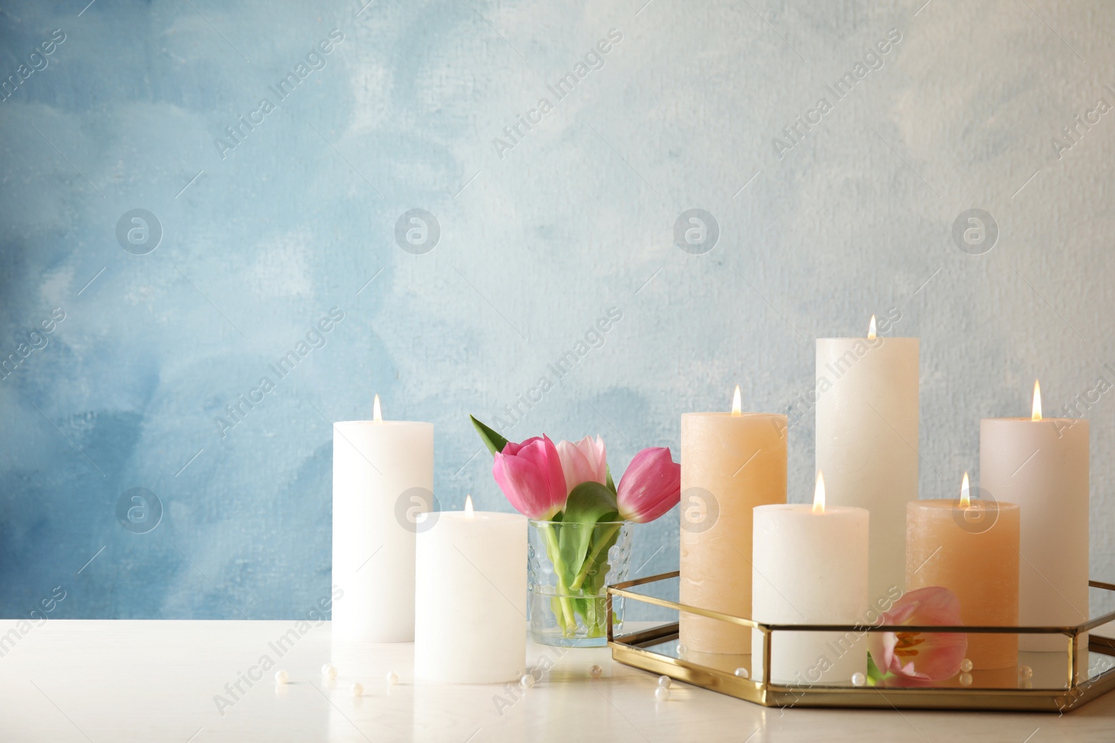 Photo of Composition with burning candles on table against color background. Space for text