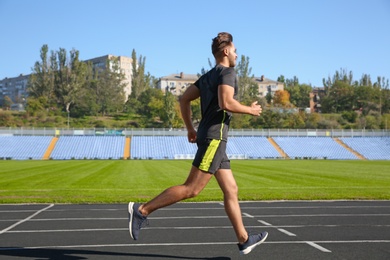 Sporty man running at stadium on sunny morning