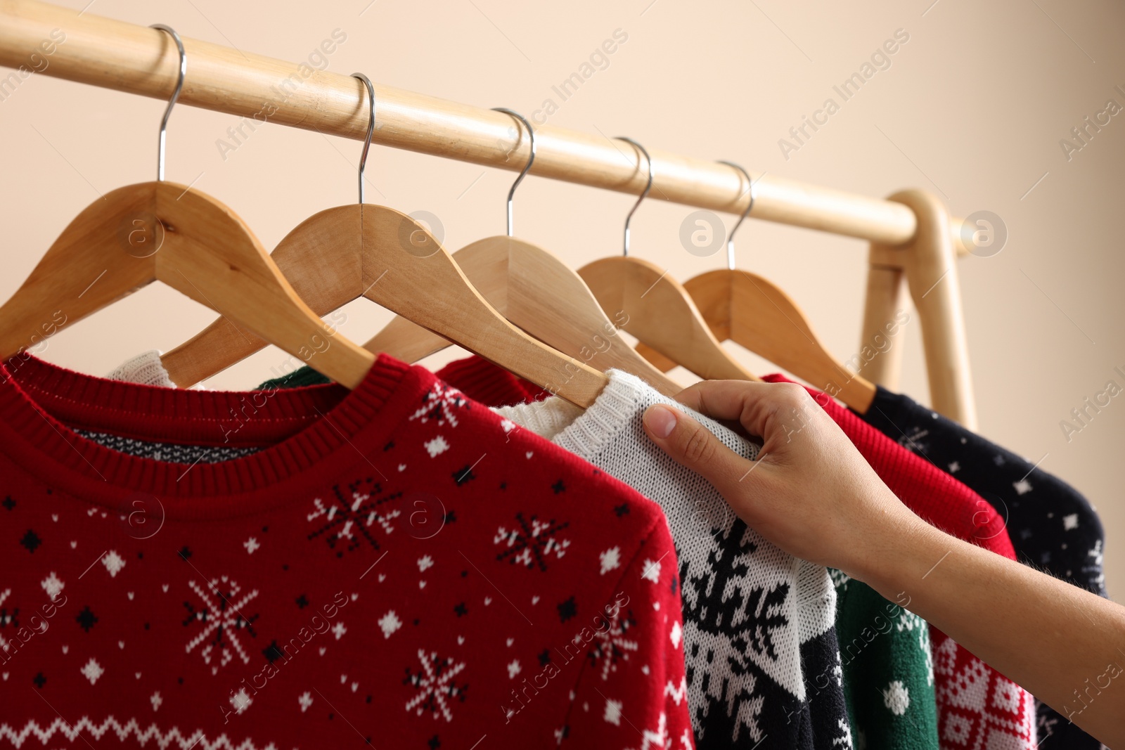 Photo of Woman choosing Christmas sweater from rack near beige wall, closeup