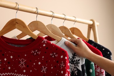 Photo of Woman choosing Christmas sweater from rack near beige wall, closeup