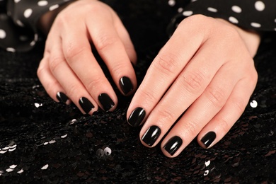Photo of Woman showing black manicure on shiny fabric, closeup. Nail polish trends
