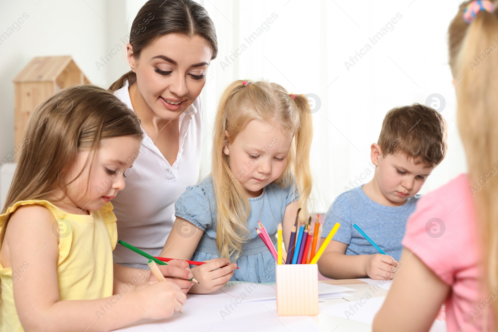 Photo of Little children with kindergarten teacher drawing at table indoors. Learning and playing